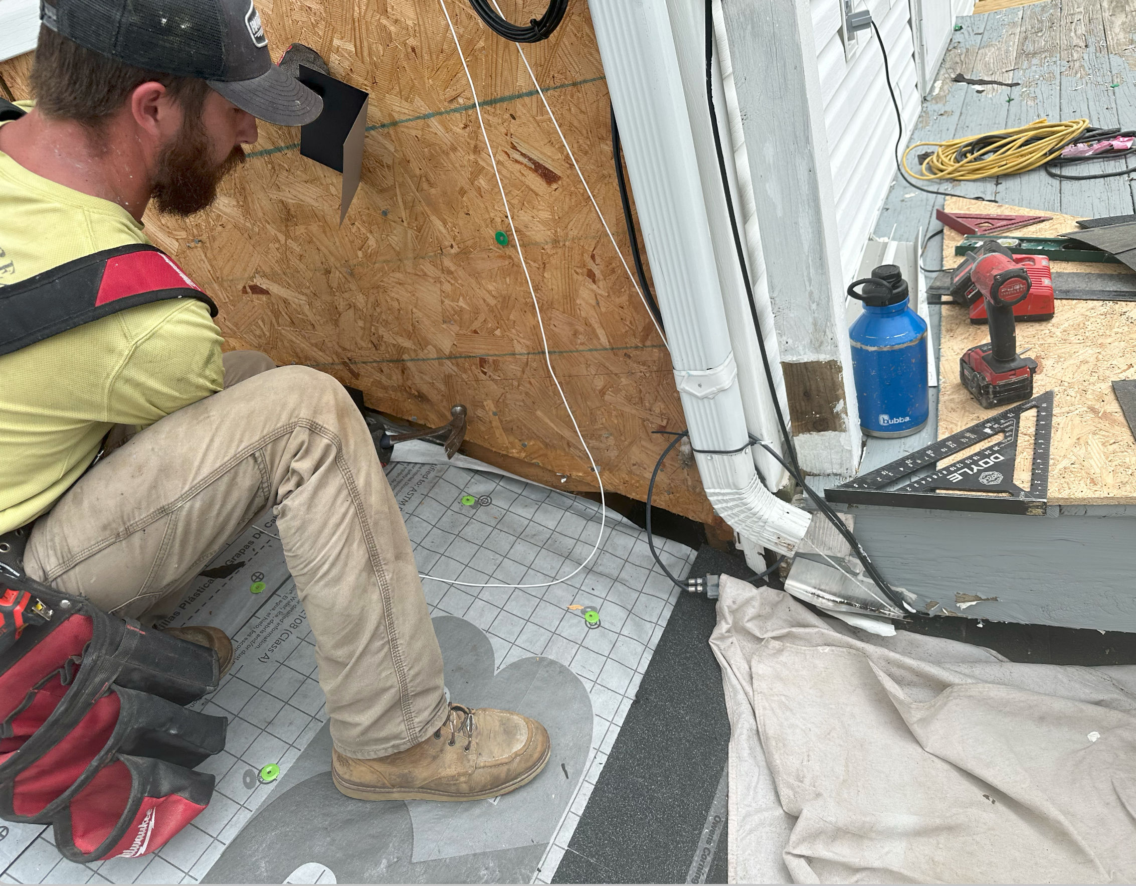 Jesse Glenn kneeling on a roof deck beside his tools, fitting flashing against the wall.
