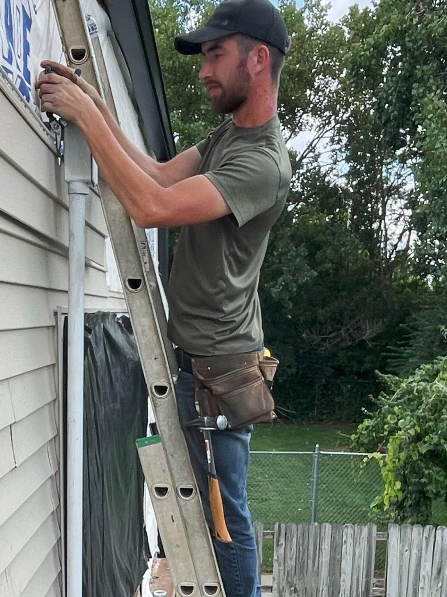 Jesse Glenn on a ladder, working on the side of a house.