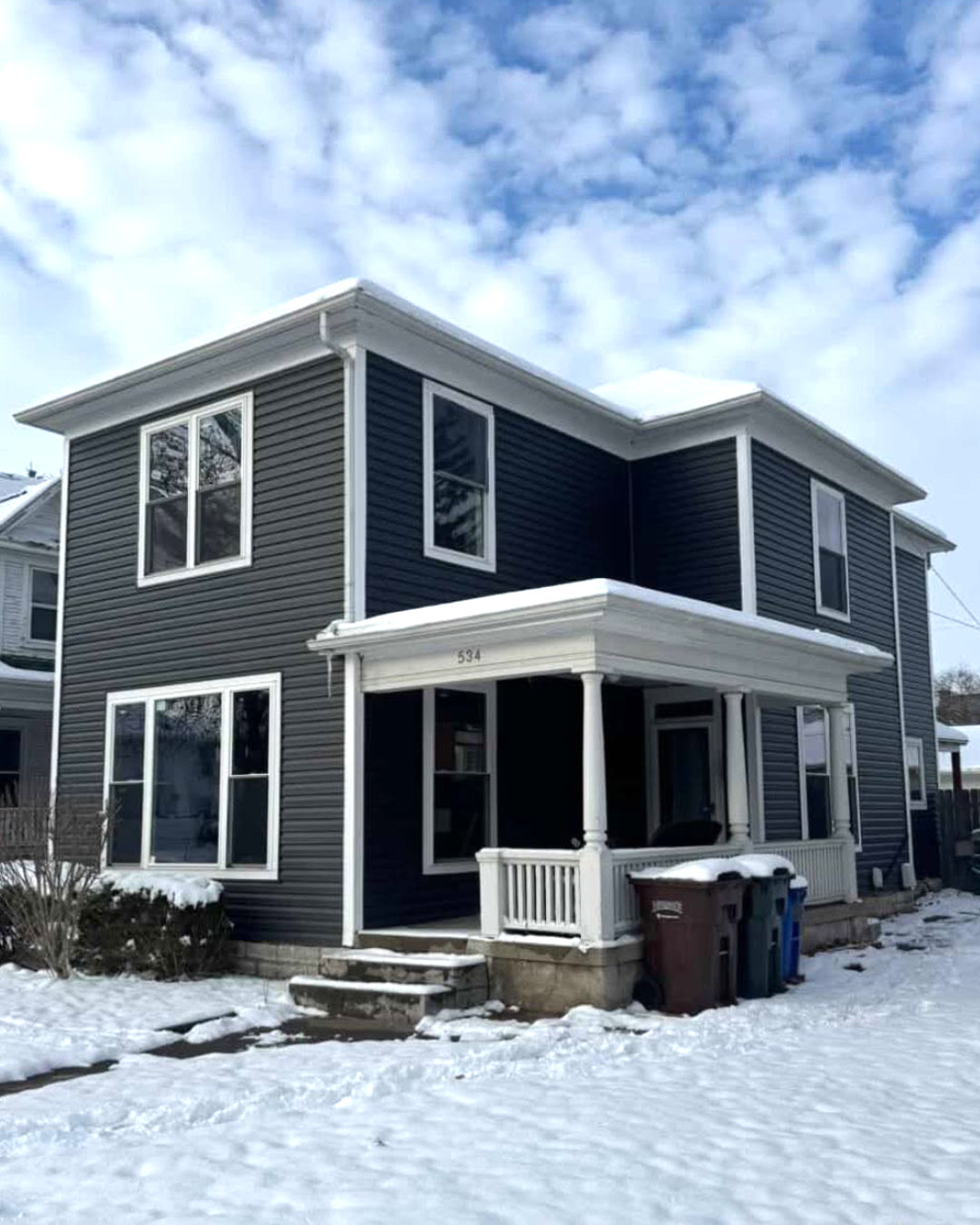 A two-story house after new siding and paint, photographed in snow.
