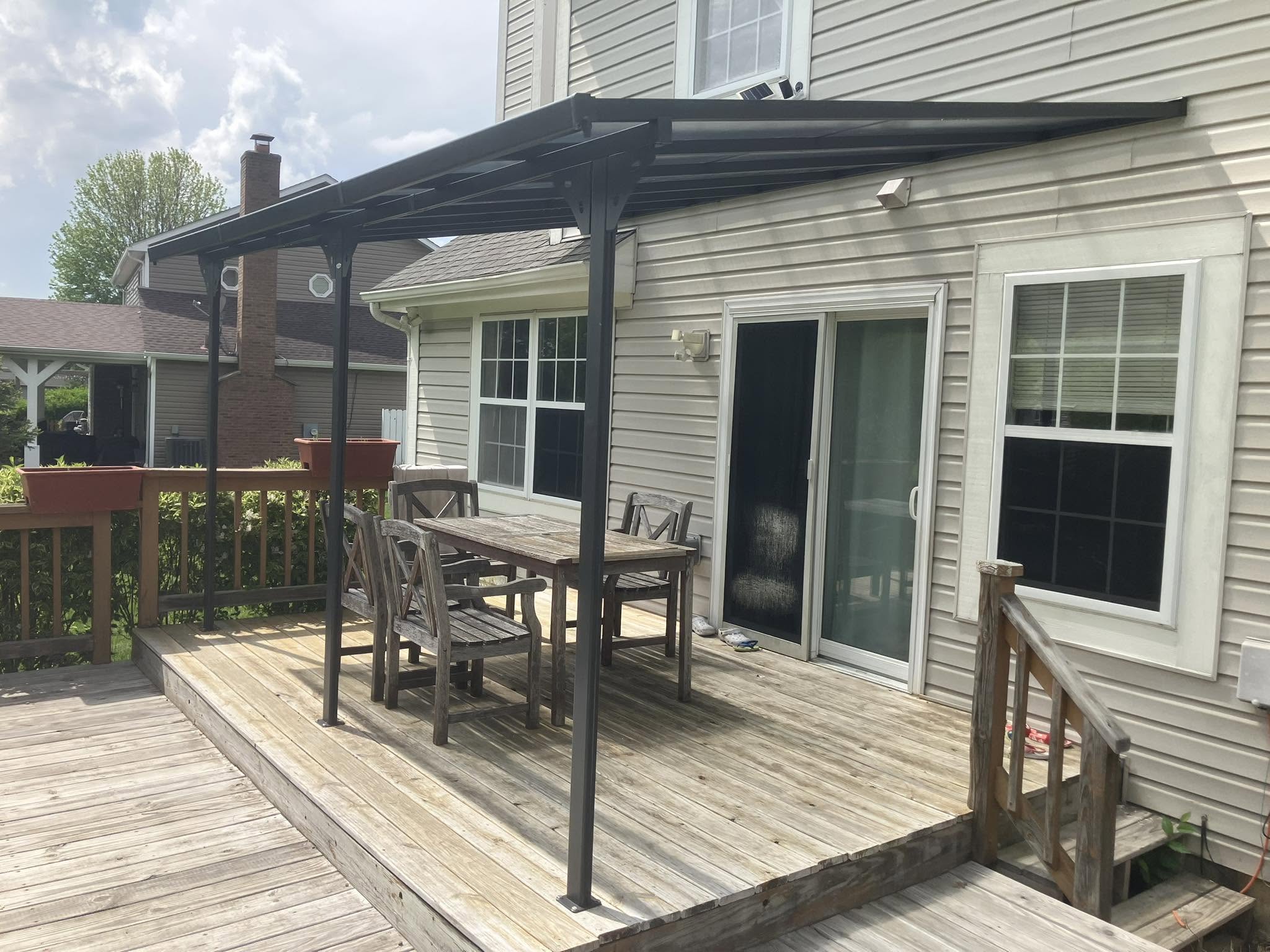 A dark metal awning over an existing wood deck with a table and chairs.