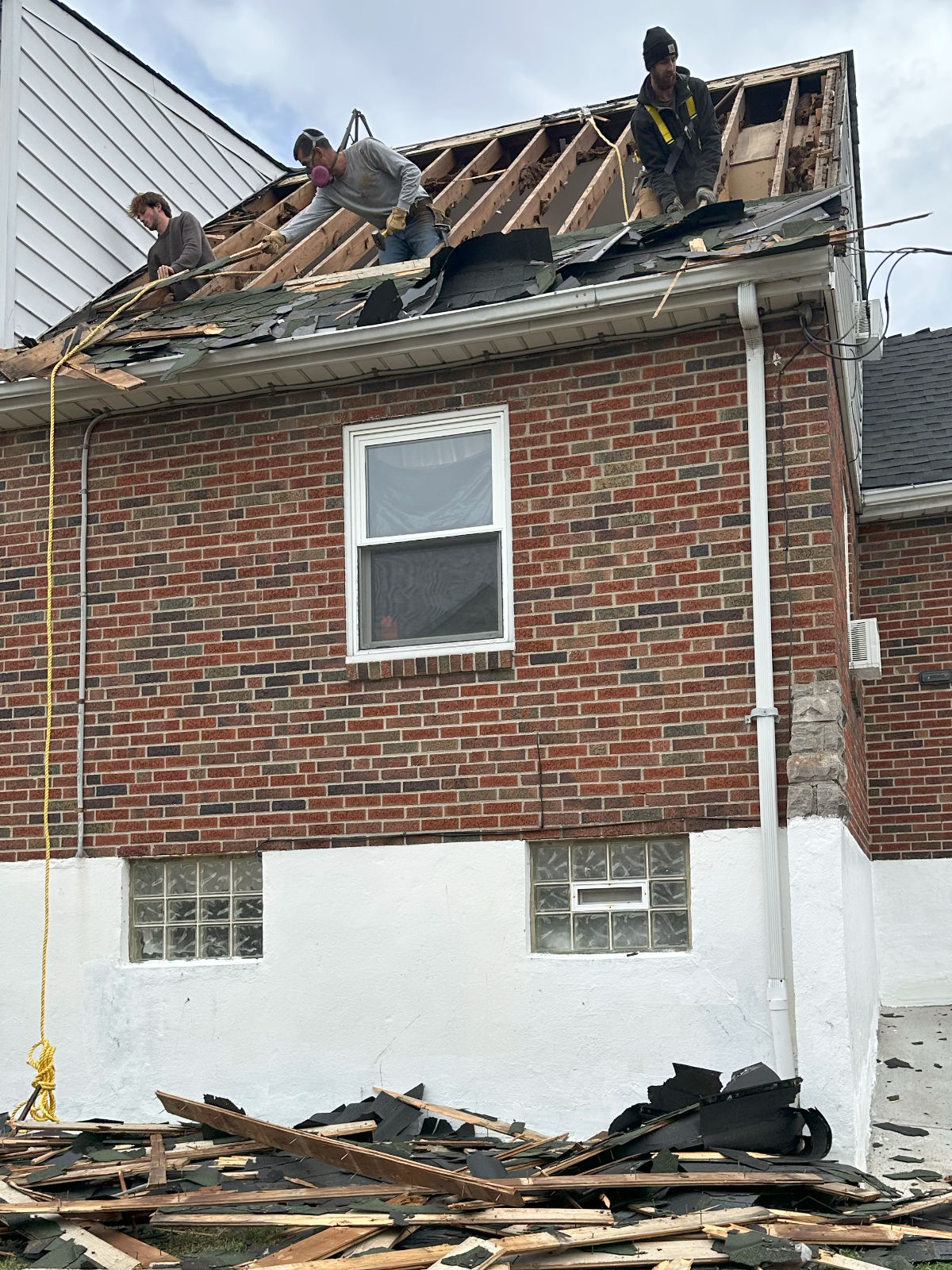 A crew stripping a roof back to the rafters on a brick house.