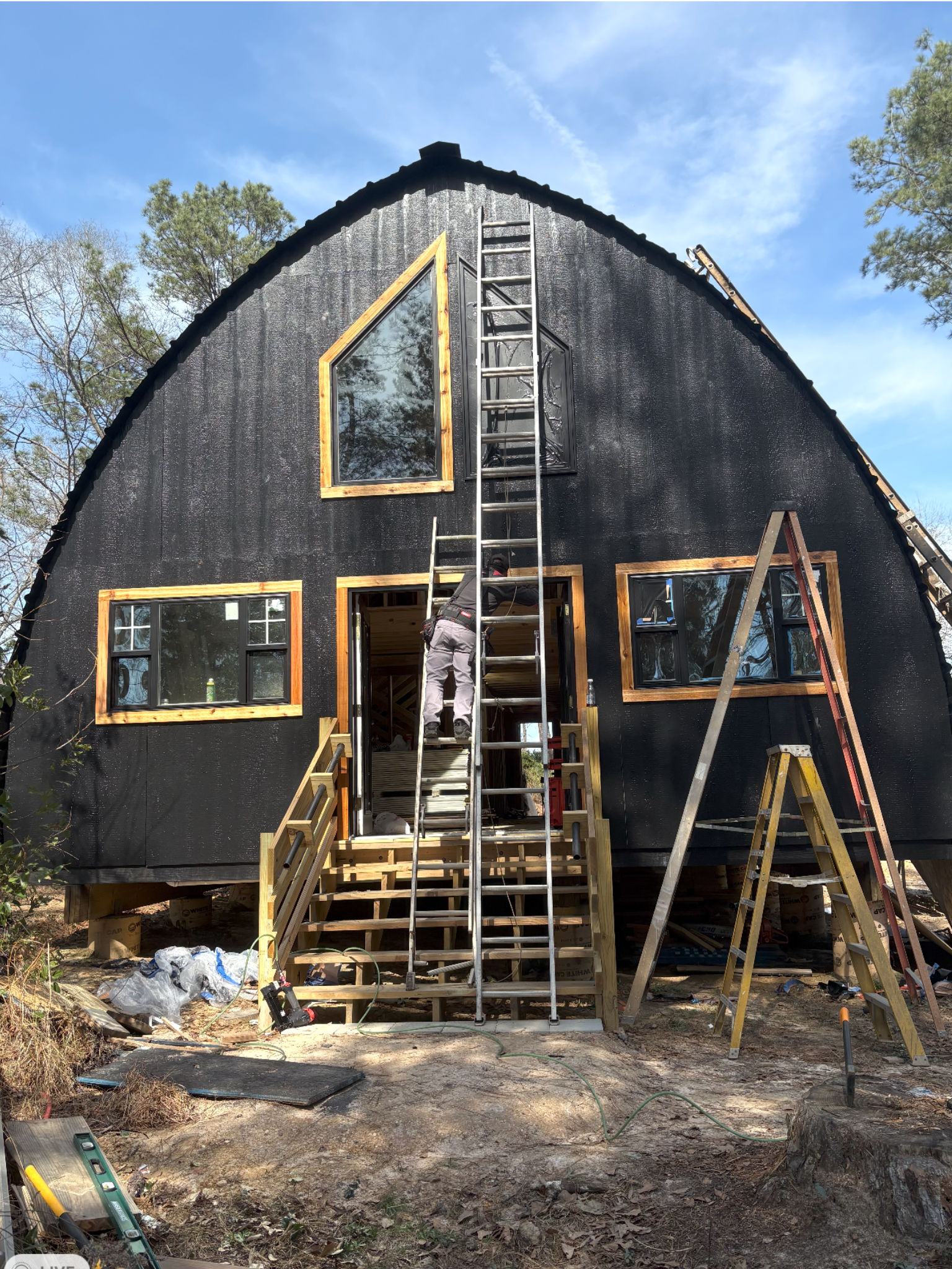 A black curved-roof cabin under construction with new windows and steps.